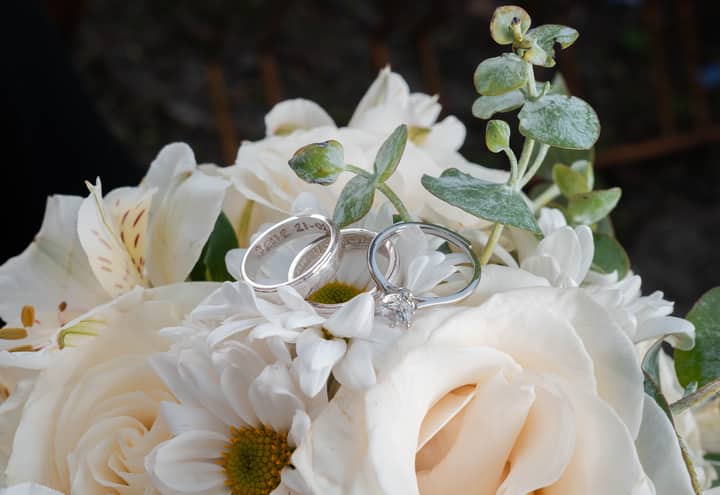 Close-up of wedding rings elegantly placed on a white floral bouquet, symbolizing love and commitment.