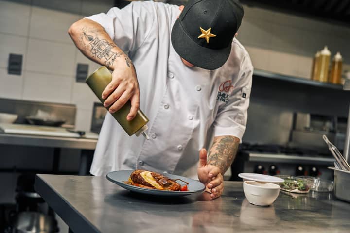 Chef garnishing a gourmet dish with sauce in a professional kitchen setting.