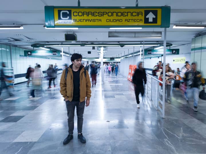 A young man stands amid a busy corridor in the Ciudad de México metro station, blending urban life with human presence.