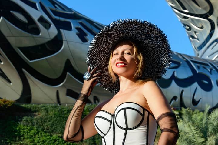 Elegant woman in a chic outfit posing beside modern architectural work outdoors.