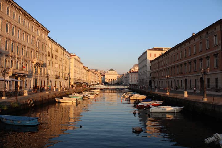 Captivating sunset over a canal in Trieste, Italy with boats lining the serene water.