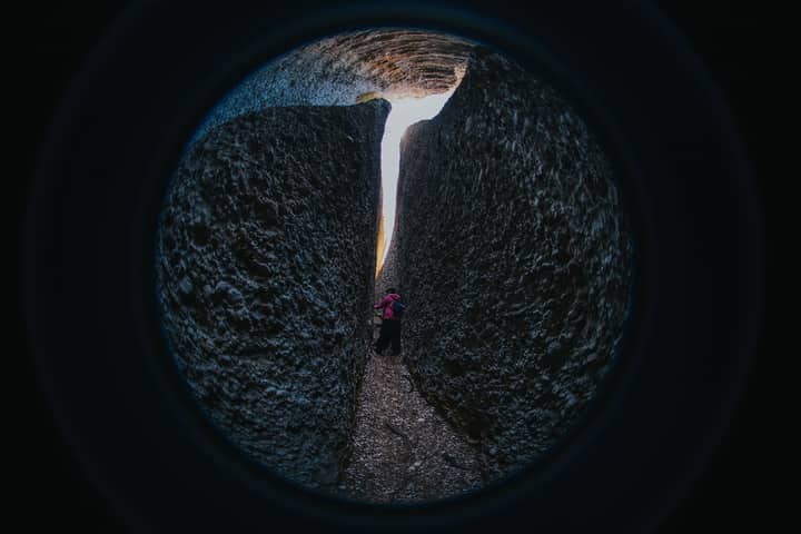 A person navigates a narrow passageway between large rock formations, captured with a fisheye lens.