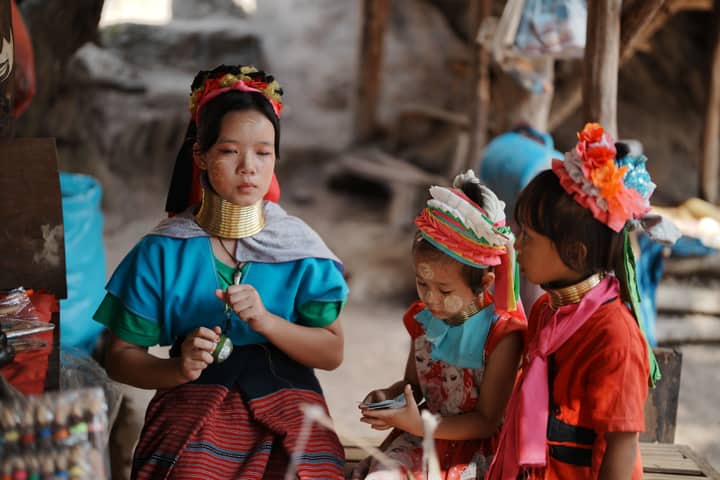 Young Long Neck Karen woman with children in traditional attire, outdoors.