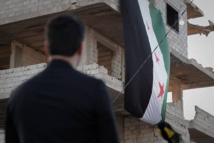 A man observes a Syrian flag draped over a war-torn building in Damascus, Syria.