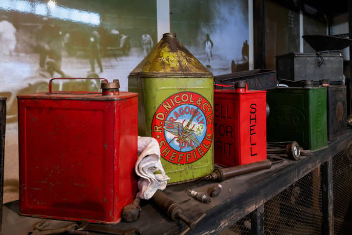 A collection of vintage oil cans on a wooden shelf in a historic garage exhibit.