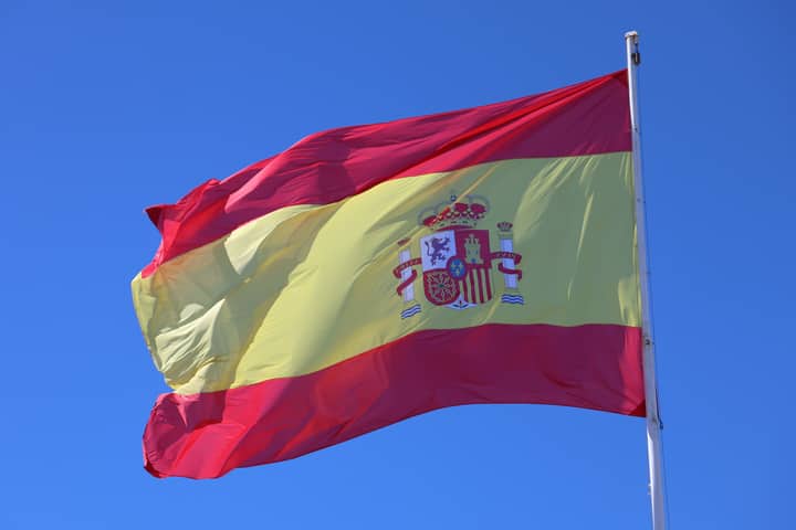 Vibrant Spanish flag waving against a clear blue sky, emblematic of national pride.