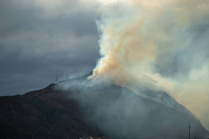 Thick smoke rises from a mountainside in Norway, creating a dramatic sky scene.