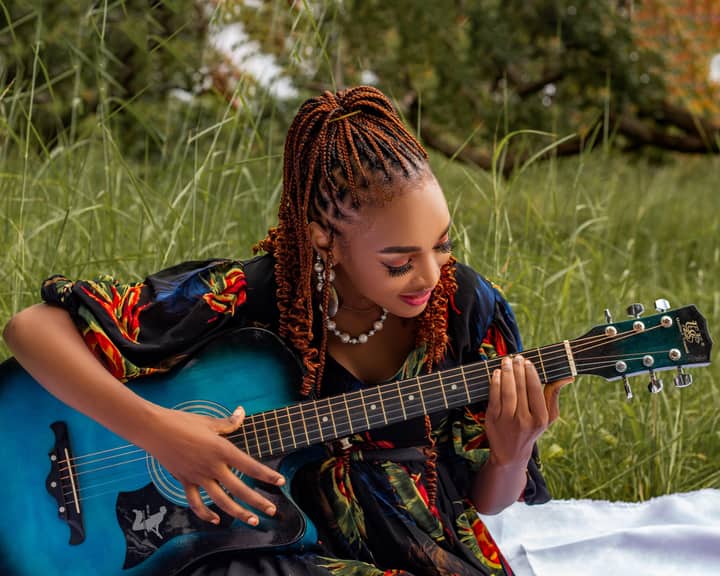 A woman enjoying playing guitar in a sunlit meadow, evoking a sense of peace and creativity.