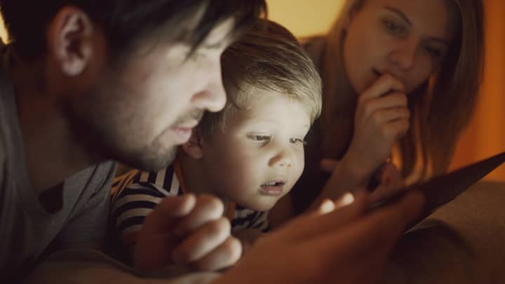 A family of three, including parents and a child, intently watching a digital tablet together indoors.