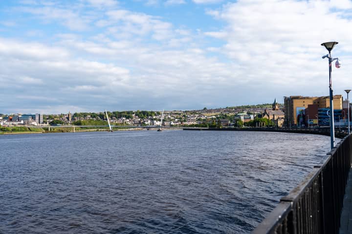 Scenic view of the Peace Bridge spanning the River Foyle in Derry, Ireland under clear blue skies.