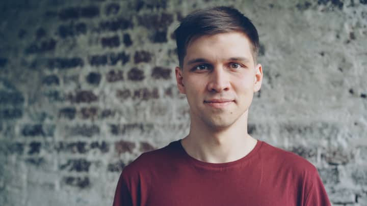 Casual portrait of a young man in a red shirt standing against a brick wall.