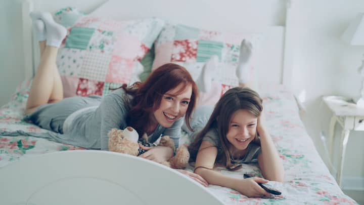 Mom and daughter lying on bed watching TV, enjoying cozy time together.