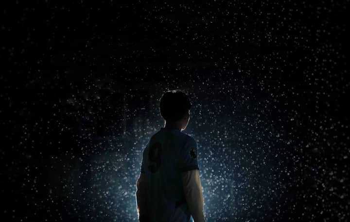 A dramatic silhouette of a soccer player standing in rain with backlit lighting.