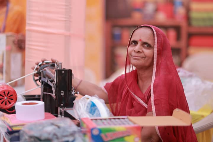 A Rajasthani woman in a red saree sewing, symbolizing empowerment and self-reliance.