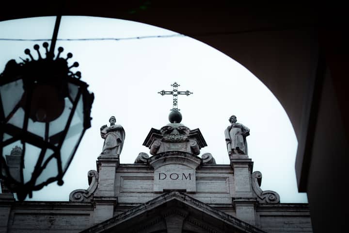 Close-up of a historic church facade in Turin, featuring statues and a cross against the sky.