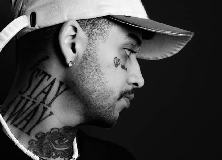 Profile portrait of a tattooed young adult wearing a cap in black and white.