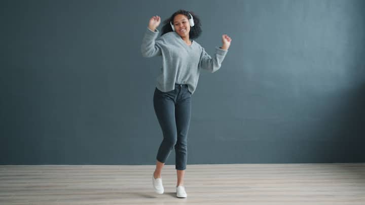 Happy young woman dancing with headphones on, enjoying music in a modern room.