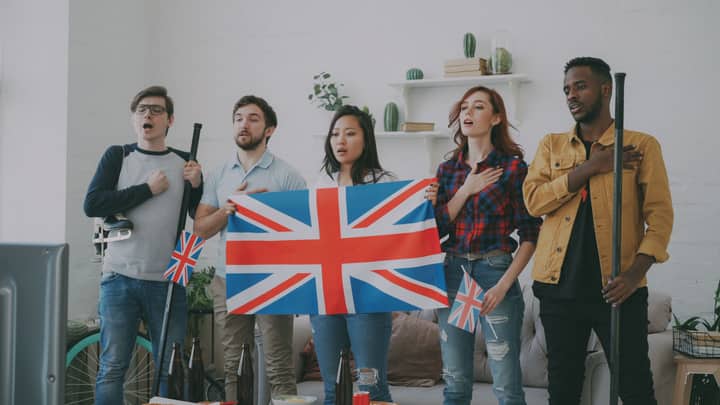A diverse group of adults perform an anthem indoors, displaying the UK flag passionately.