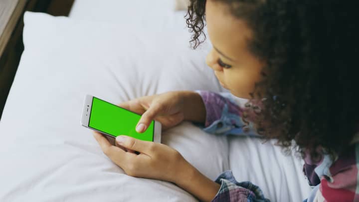 Teenager holding smartphone with chroma key screen in cozy setting.