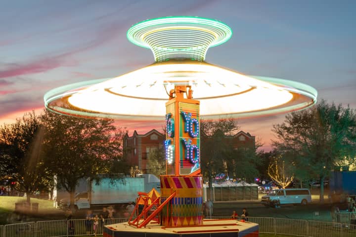Vibrant spinning carousel at a carnival with a stunning sunset backdrop.