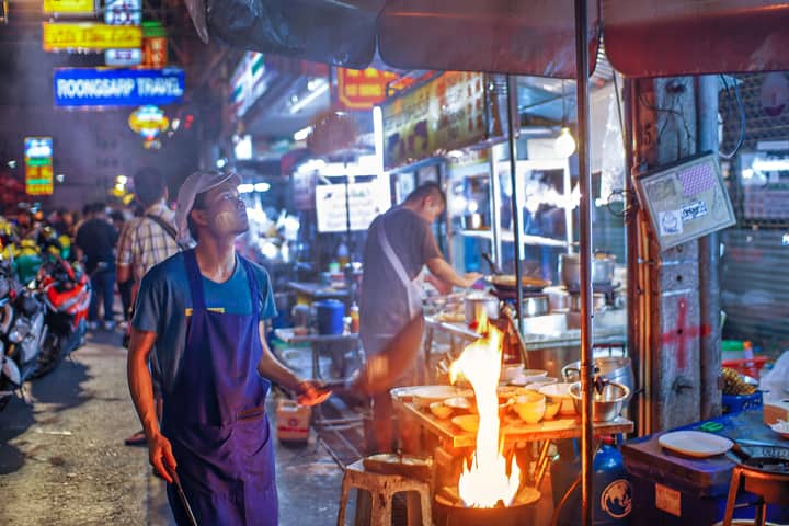 A lively street food vendor in Bangkok bustling with night activity and colorful lights.