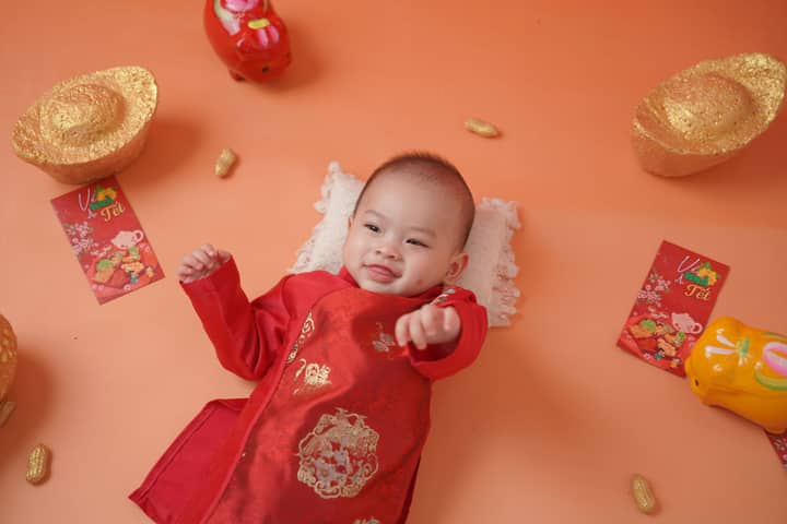 Smiling baby dressed in traditional attire for Lunar New Year surrounded by festive decorations.