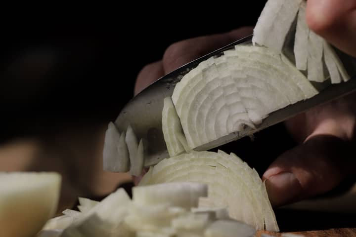 Detailed shot of slicing white onions with a sharp knife, perfect for cooking themes.