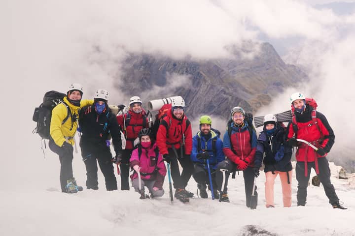 A group of climbers poses atop a snowy mountain during a cloudy day, showcasing adventure.