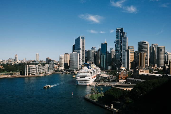 Aerial view of Sydney skyline with a cruise ship docked at the harbor under a clear blue sky.