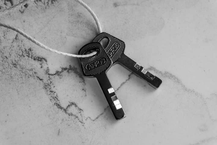 Black and white close-up of two keys tied with string on a textured marble surface.