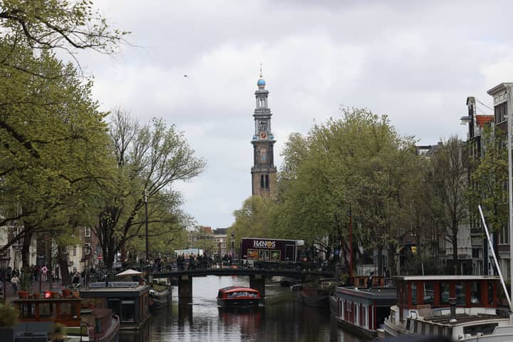 Scenic view of Amsterdam's Westerkerk tower and canal with boats and greenery in spring.