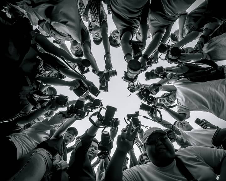 A diverse group of photographers pointing cameras, captured from below, creating a powerful visual impact.