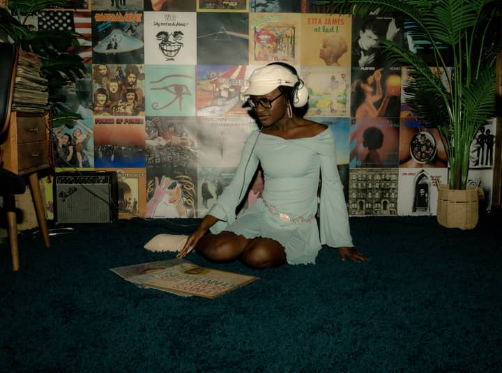 A person enjoying vinyl records in a vintage-themed room with classic album covers on the wall.
