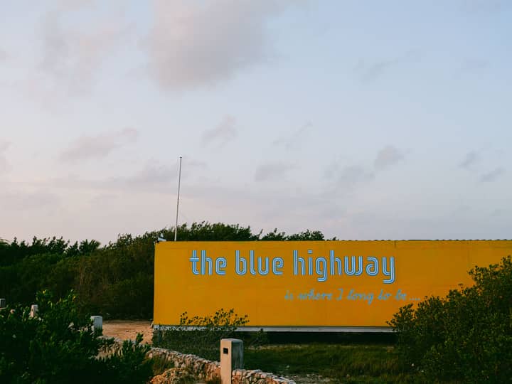 Yellow billboard with 'the blue highway' text against serene outdoor backdrop.