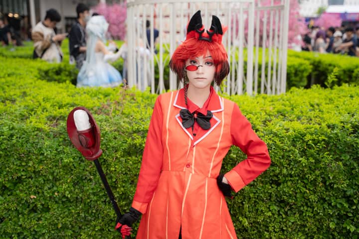A person in cosplay with a red costume poses confidently in an outdoor garden.