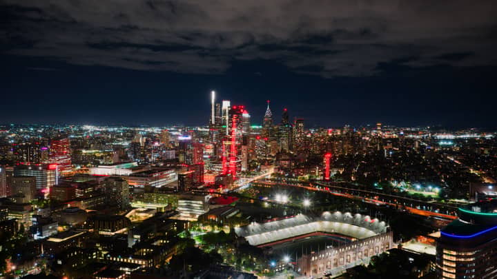 A breathtaking aerial view of Philadelphia's illuminated skyline at night, highlighting the vibrant cityscape and a prominent stadium.