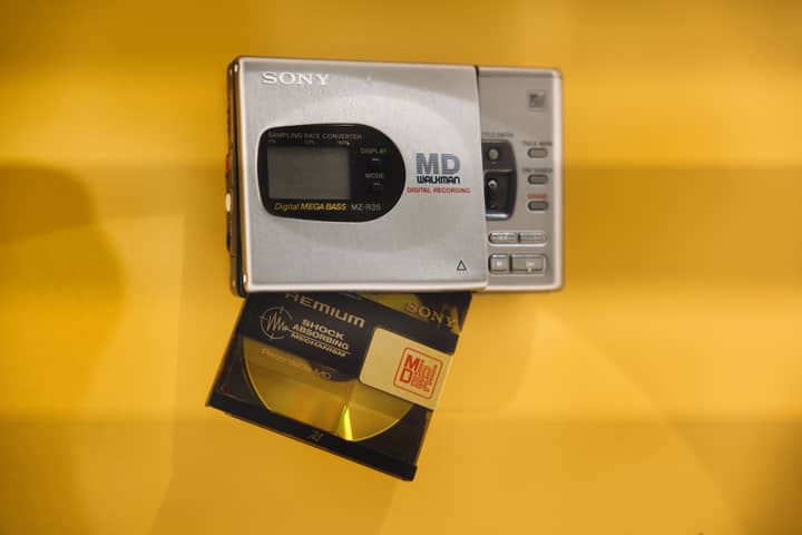 Close-up of a vintage Sony MiniDisc player and disc on a bright yellow background.