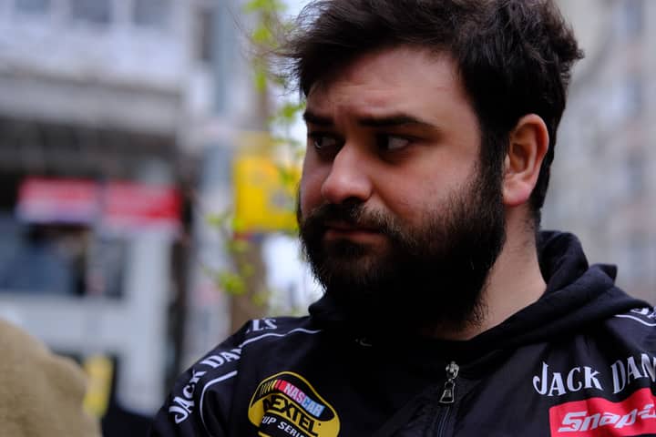 A thoughtful man looking aside in an urban setting, wearing a branded black jacket.