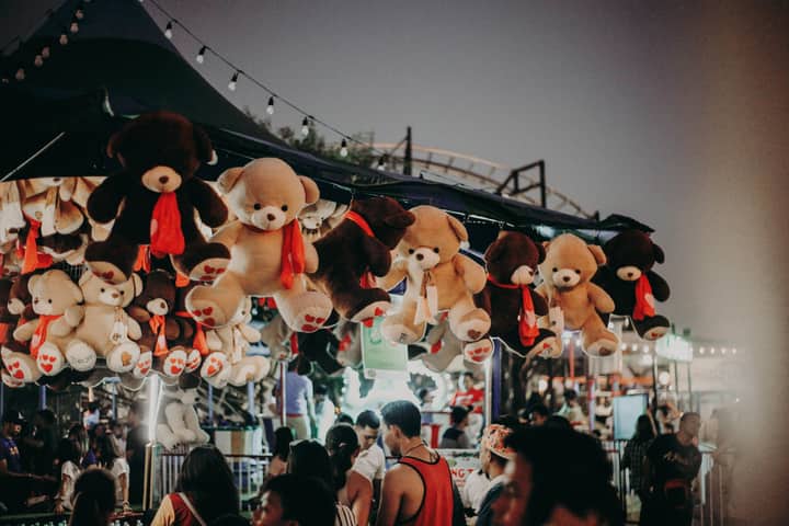 A bustling carnival scene at night featuring teddy bear prizes and a lively crowd.