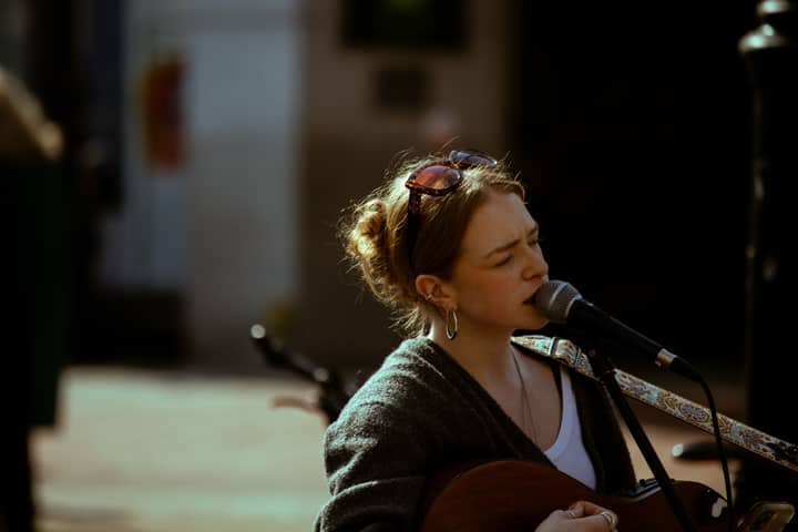 A female street musician performs outdoors with a guitar and microphone in Ireland.