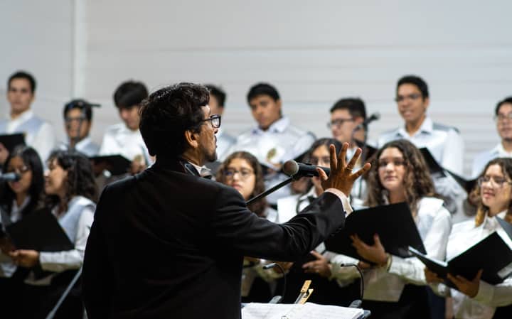 A university choir performing indoors under the direction of a conductor during a ceremony in Piura, Peru.