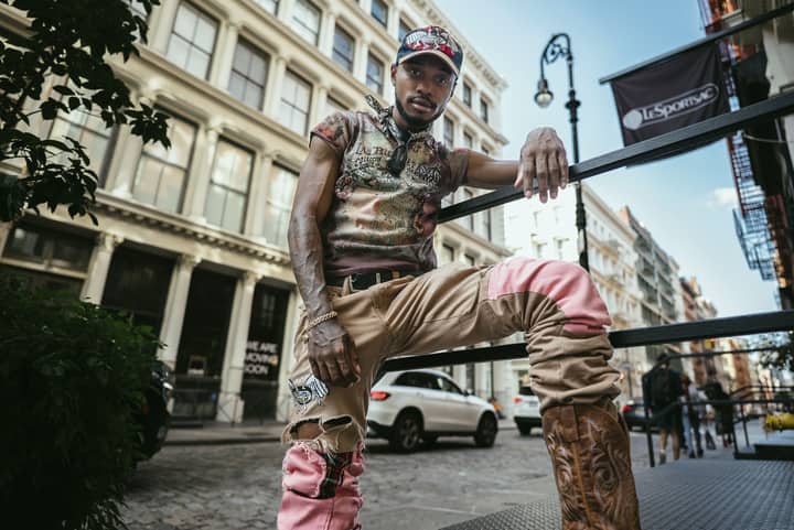 Fashionable young man in trendy attire poses on a city street in Soho, NYC, showcasing urban style.