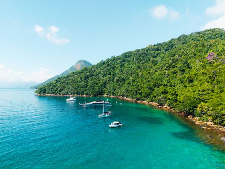 Stunning aerial shot of clear turquoise waters and moored boats along Ilha Grande's lush coastline in Brazil.