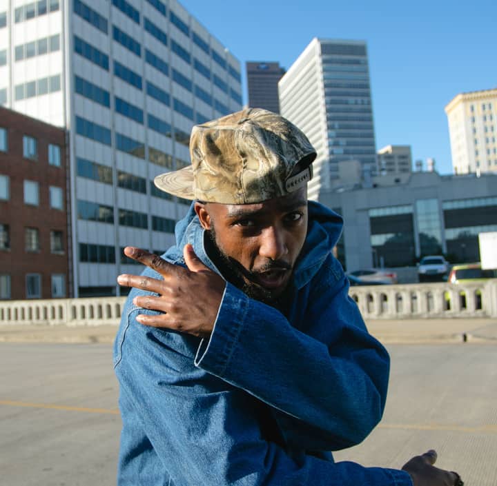 Dynamic street portrait of a young man in denim and camouflage cap posing confidently outdoors.