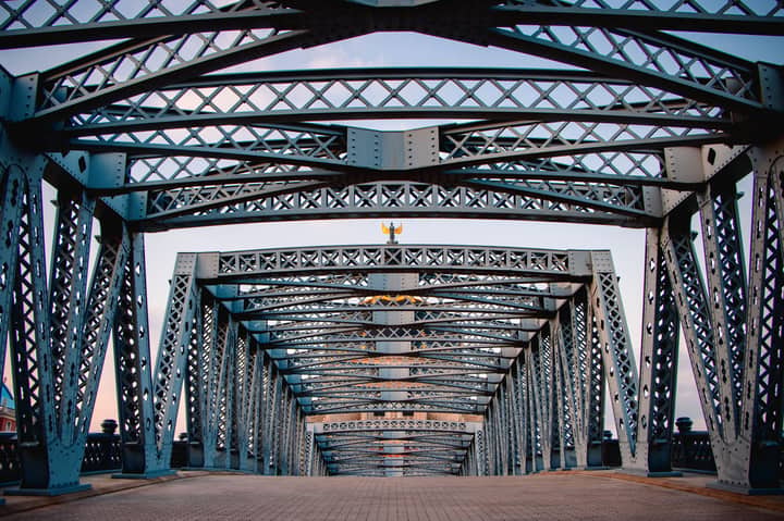 Symmetrical view of an iron truss bridge with intricate metalwork at twilight.