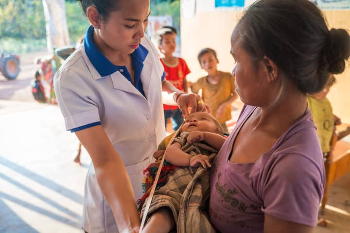 Healthcare worker assisting mother with infant in rural Laos clinic.