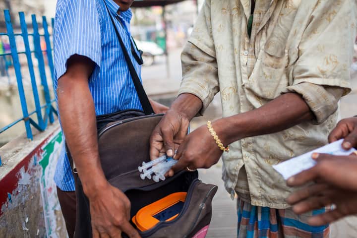 A man exchanges needles on a street in Dhaka, Bangladesh, highlighting public health efforts.