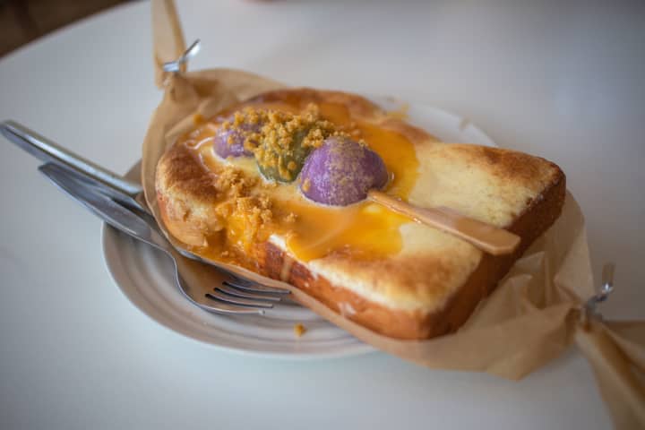 Close-up of a sweet toast topped with vibrant spreads and crumbles, served on a white plate.