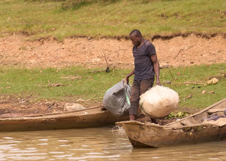 A man balances bags into a wooden canoe on a riverbank in Minna, Nigeria.