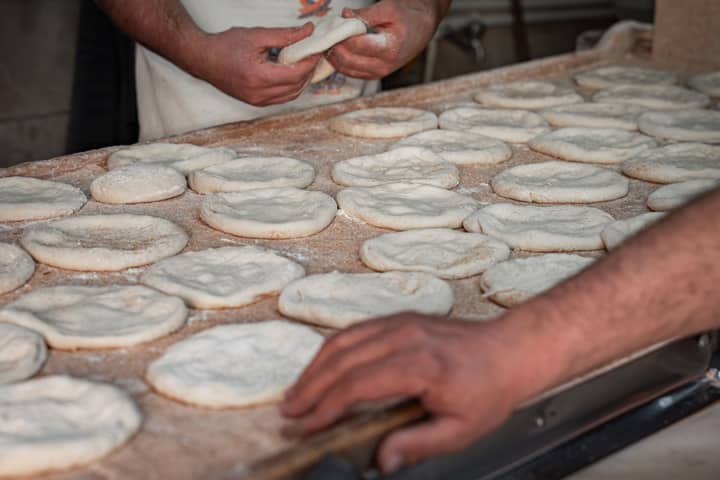 Artisan bakers shaping fresh pita bread dough by hand in a traditional bakery setting.